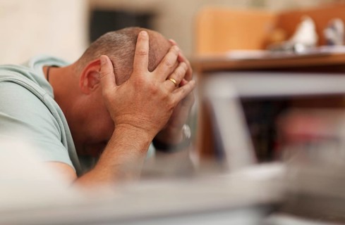 Worried businessman sitting in front of his computer with his head in his hands