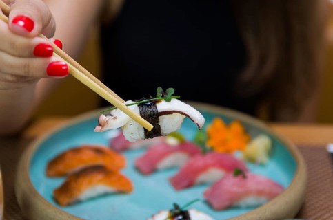 Woman eating delicious sushi, closeup on chopsticks