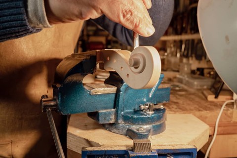 Italian luthier is meticulously shaping the scroll of a violin using a gouge, with the piece