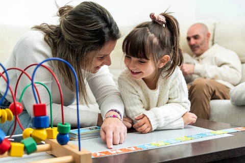 Happy family playing with alphabet puzzle, mother teaching daughter letters, father watching them,