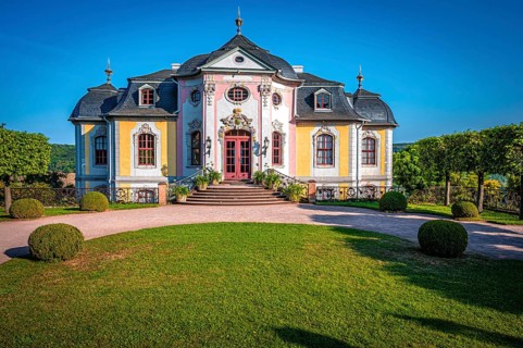 The rococo castle of the Dornburg Castles with manicured lawn and symmetrical trees against a clear