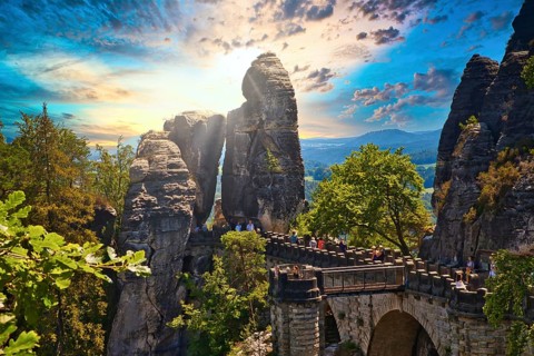 Stone Bastei Bridge connects imposing rocks at sunset, surrounded by lush trees, Elbe Sandstone