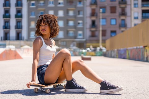 Stylish young woman taking a break, sitting on her skateboard in a skate park, enjoying the urban