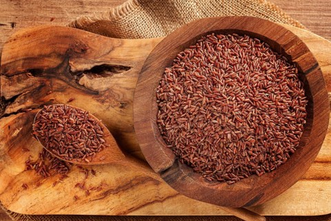 Natural, red rice, in a wooden bowl and spoon on a wooden surface in rustic style, top view