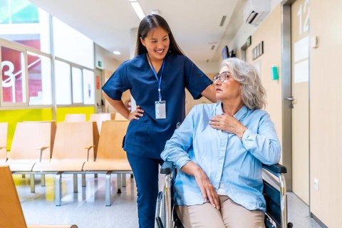 Young nurse assisting and comforting a senior woman in a wheelchair in a hospital waiting room