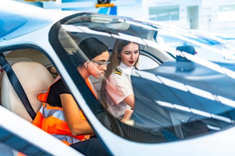 Two female pilots, one in uniform and the other in a safety vest, collaborate inside an aircraft