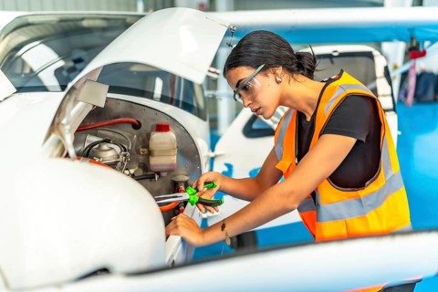 Young woman aircraft mechanic wearing safety glasses and high visibility vest using pliers while
