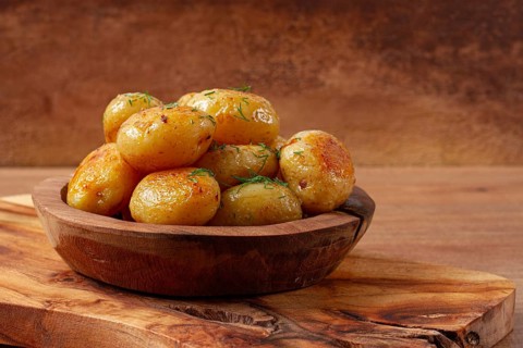 Baked new potatoes, with butter and dill, on a wooden plate, homely, rustic, no people