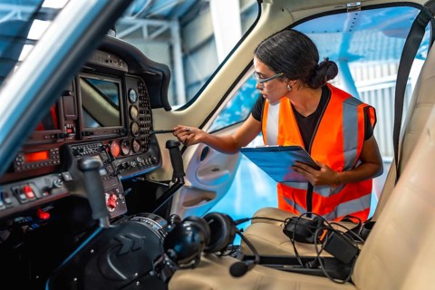 Female aircraft maintenance engineer using checklist while inspecting control panel inside cockpit