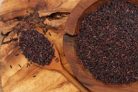 Natural black rice in a wooden bowl and spoon on a wooden surface in rustic style, top view