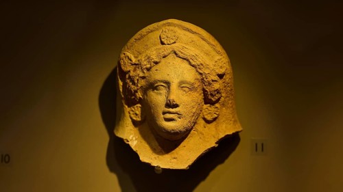 Ancient stone head of a goddess, exhibited in a museum-like setting, found in the cave of Aspri
