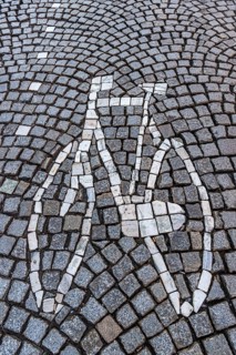 A bicycle mosaic is skilfully integrated into a street of paving stones, traffic, bicycle road,