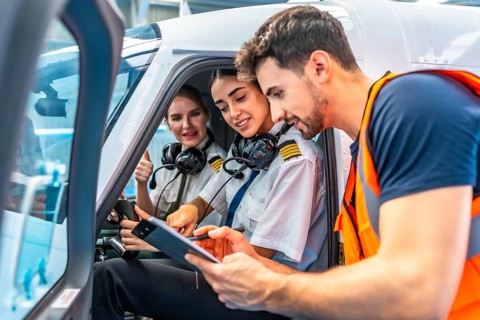 Airplane maintenance engineer briefing two smiling female pilots showing thumbs up sitting inside