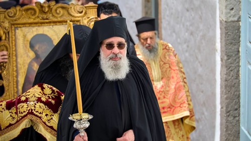 A priest in a black robe carries a candle next to an icon during a religious procession, Orthodox