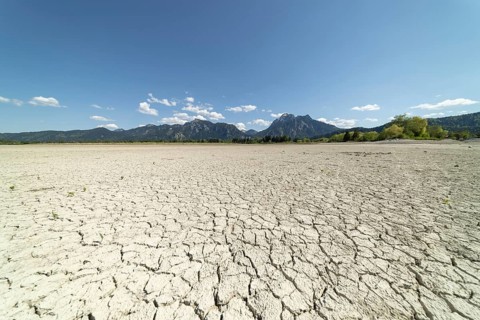 Cracked, dried out ground, waterless Forggensee in spring, behind it Tegelberg massif and Säuling,