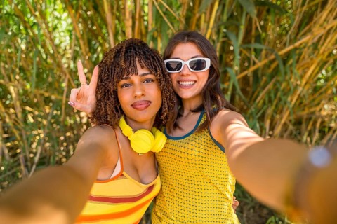 Two happy young women with headphones and sunglasses taking a selfie in a bamboo forest, one of