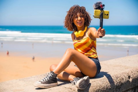 Influencer filming a vibrant vlog on a stunning beach, capturing moments with a smartphone and an
