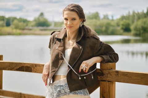 A model stands confidently near a tranquil water body, showcasing a fashionable outfit complete