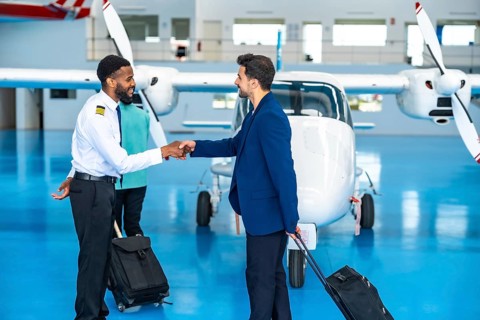 African pilot shaking hands with a businessman inside an aircraft hangar, both holding trolley