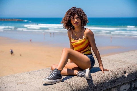 Stylish young woman wearing casual summer clothes sits on a beach wall, enjoying the ocean view