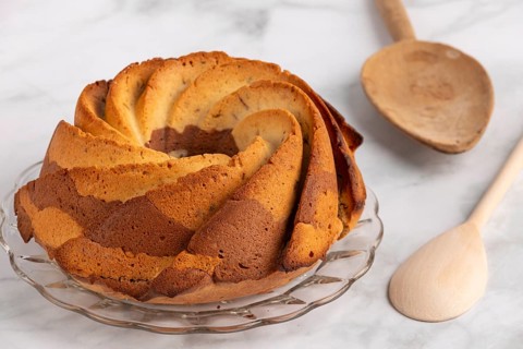 Fresh marble bundt cake, cake next to a rustic wooden spoon on a light-coloured background