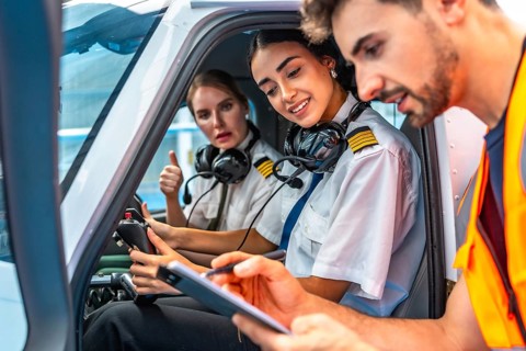 Ground crew writing on clipboard while explaining pre flight checklist to two smiling female pilots