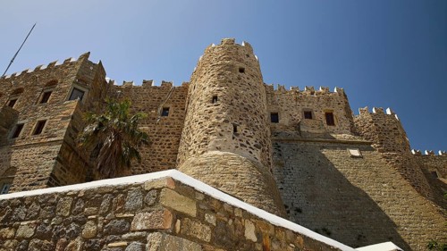 Medieval stone castle with palm trees and blue sky, imposing architecture, Monastery of St John the