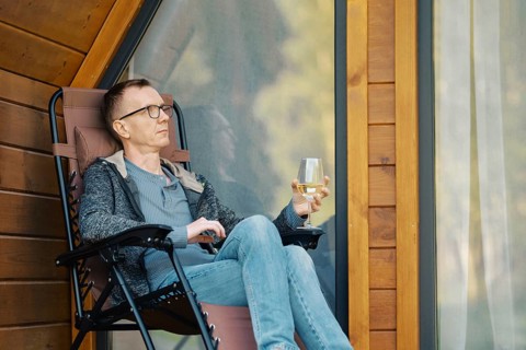 Middle-aged man relax on terrace of a tiny house with a glass of wine