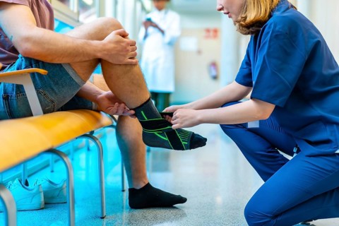 Female nurse bandaging a male patient's injured ankle in a hospital setting, providing support and