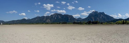Cracked, dried out ground, waterless Forggensee in spring, behind it Tegelberg massif and Säuling,