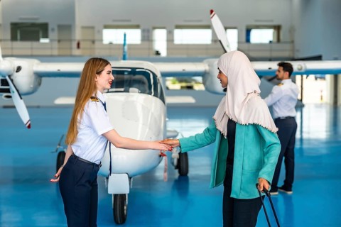 Female pilot shaking hands with a muslim businesswoman inside an aircraft hangar, symbolizing