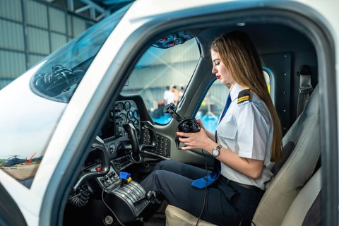 Female pilot sitting in the cockpit of a small airplane and preparing her headset, ready for
