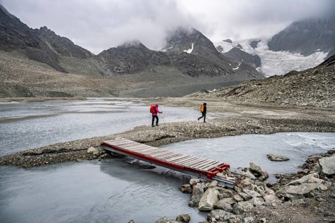 Mountaineers at a makeshift bridge over a stream, glacier river at the Glacier de Cheilon, in the