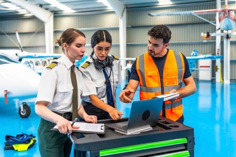 Aircraft maintenance engineer showing data on laptop to two female pilots in hangar, discussing