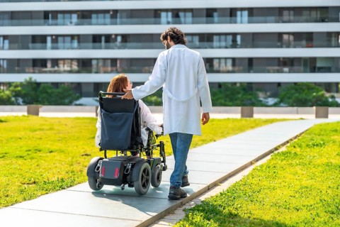Doctor assisting a female patient in a wheelchair, strolling through a modern hospital's green