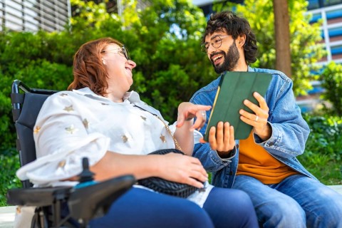 Happy woman with disability using tablet with her friend, modern lifestyle and inclusion concept,