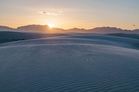 Rays of light over the mountains highlight windblown sand at sunset at White Sands National Park in