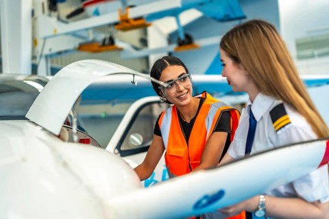 Female pilot and aircraft maintenance technician working together in hangar, discussing maintenance