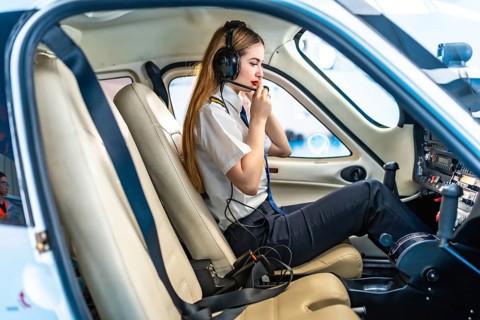 Female pilot sitting in the cockpit of a small aircraft, wearing a headset and communicating,