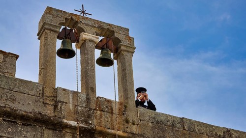 Priest next to bells on a wall in front of a blue sky, Monastery of St John the Theologian,