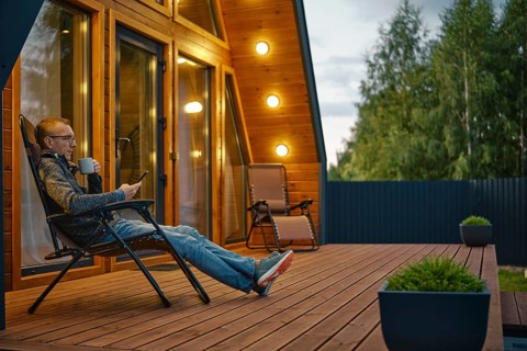 Middle-aged man sits with a cup of tea in the evening on the terrace illuminated by outdoor wall