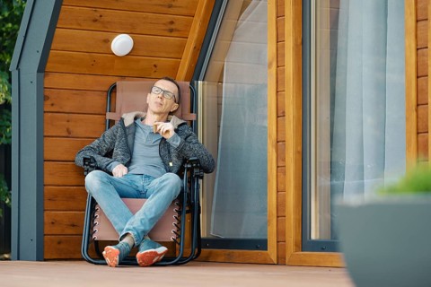 Middle-aged man enjoys a cigar while lounging in a chair on the terrace of a log cabin