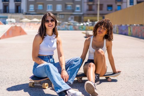 Two young women are sitting on their skateboards in a skate park, enjoying a break and smiling