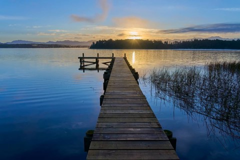 Wooden jetty reaches into the lake as the sunrise illuminates the dawn on Lake Mahinapua, Ruatapu,