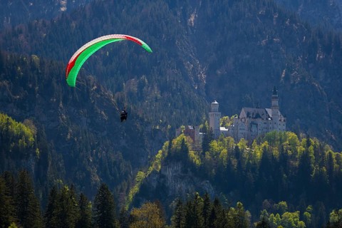 A paraglider flies high above Neuschwanstein Castle in the mountains, Schwangau near Füssen,