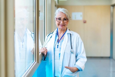 Portrait of a confident senior female doctor standing in a bright hospital corridor, representing