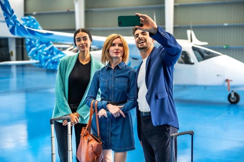 Three businesspeople are taking a selfie with a smartphone in a hangar with a private jet and