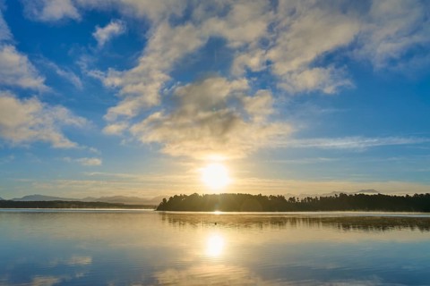 Sunlight breaks through the clouds in the morning over a calm lake, Lake Mahinapua, Ruatapu, South