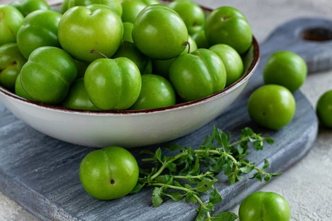 Tkemali, green cherry plum, in a bowl, on a gray table, top view, natural light, no people