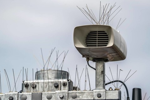 Loudspeakers on a scoreboard, at a railway station, studded with thin wires against birds, pigeons,